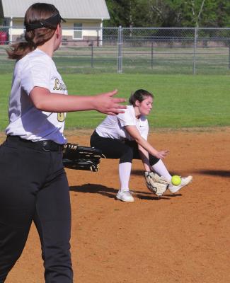 HUGO LADY BUFFALO SHORTSTOP KENDELL HICKS hustles to scoop up a hard-hit ground ball to her position and make the out at first base during home field action against Rock Creek Friday. Standing by at her third base position to assist for the Lady Buffaloes is Brinlee Allensworth. Hugo News Photo / Stan Stamper