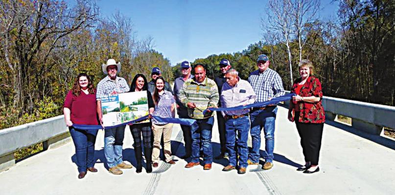CHOCTAW COUNTY COMMISSIONER Ronnie Thompson cuts a ribbon Nov. 15 in celebration of the completion and opening of the new Muddy Boggy Creek bridge north of Boswell. Standing to Thompson’s right is his uncle, Perry Thompson, who represents Choctaw Nation Tribal Council District 8. Also pictured are other county officials, Choctaw Nation representatives and Guy Engineering employees. Photo Courtesy / Sonya Campbell
