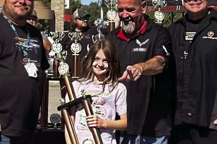 BRIAR McCLURE is all smiles as she hoists the massive trophy claimed by her father Brian (center) at the recent Classic Car Fest hosted by the Choctaw Nation Casino in Grant. Also pictured are Will Payne (right) and Casino representative Phillip Baker.