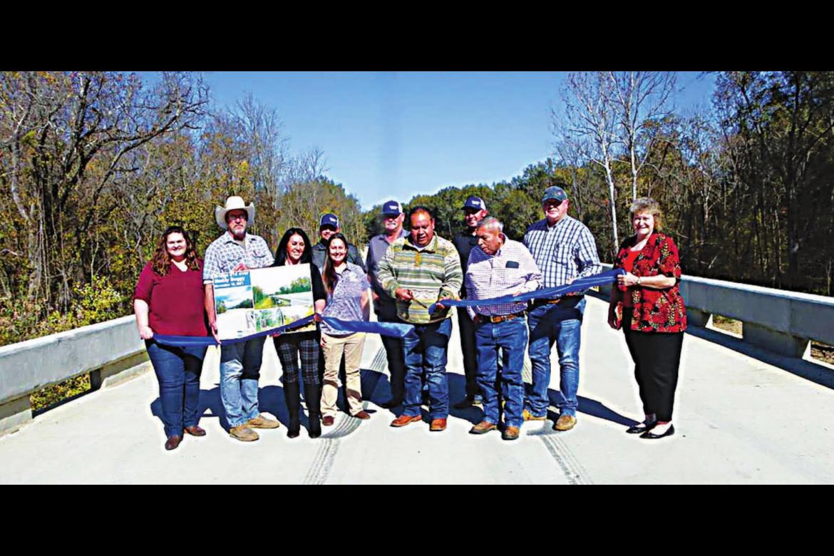 CHOCTAW COUNTY COMMISSIONER Ronnie Thompson cuts a ribbon Nov. 15 in celebration of the completion and opening of the new Muddy Boggy Creek bridge north of Boswell. Standing to Thompson’s right is his uncle, Perry Thompson, who represents Choctaw Nation Tribal Council District 8. Also pictured are other county officials, Choctaw Nation representatives and Guy Engineering employees. Photo Courtesy / Sonya Campbell